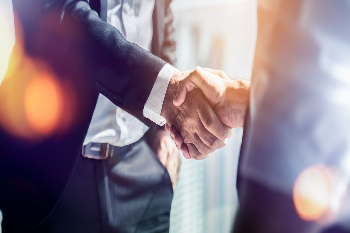 Two people in suits shaking hands with bright light effects.