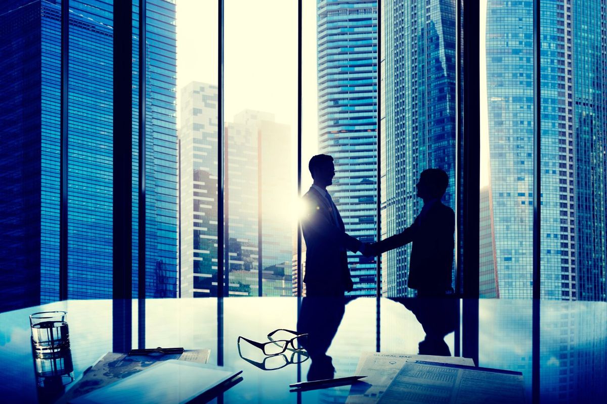 Two people shaking hands in office with city skyline view.