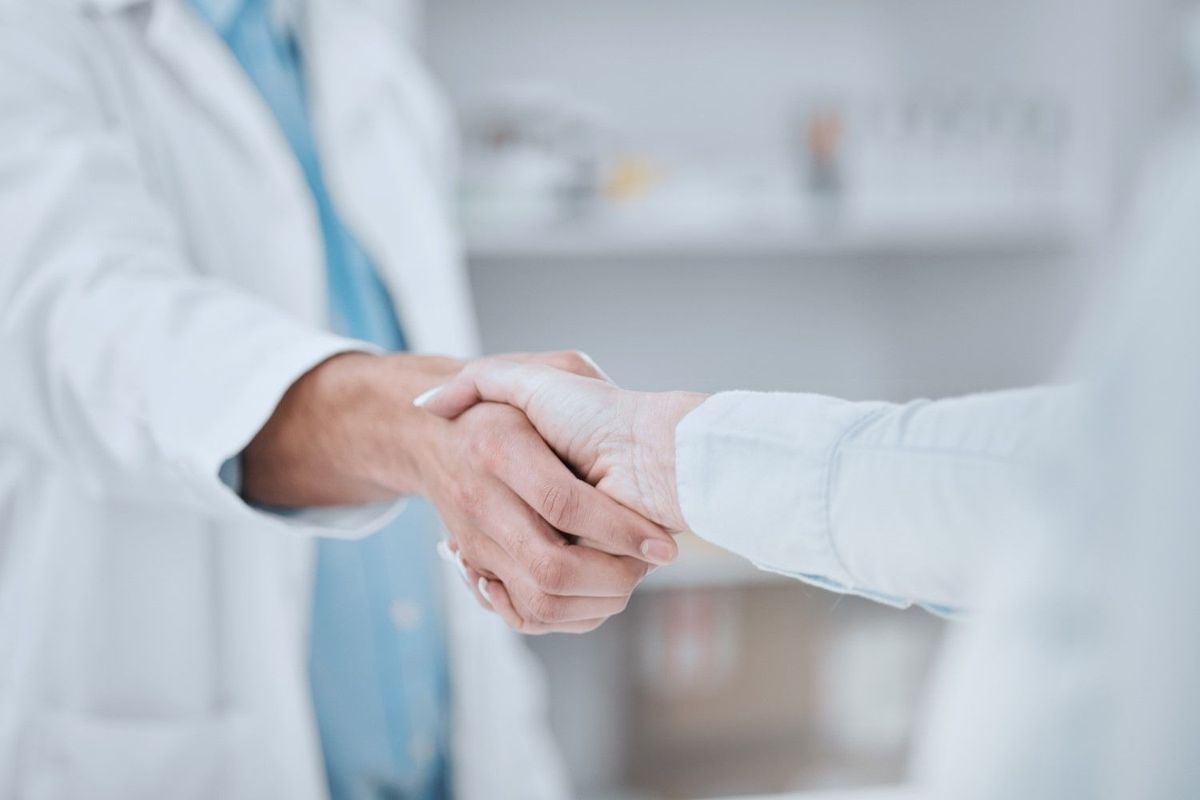 Two people wearing lab coats shake hands in business agreement.