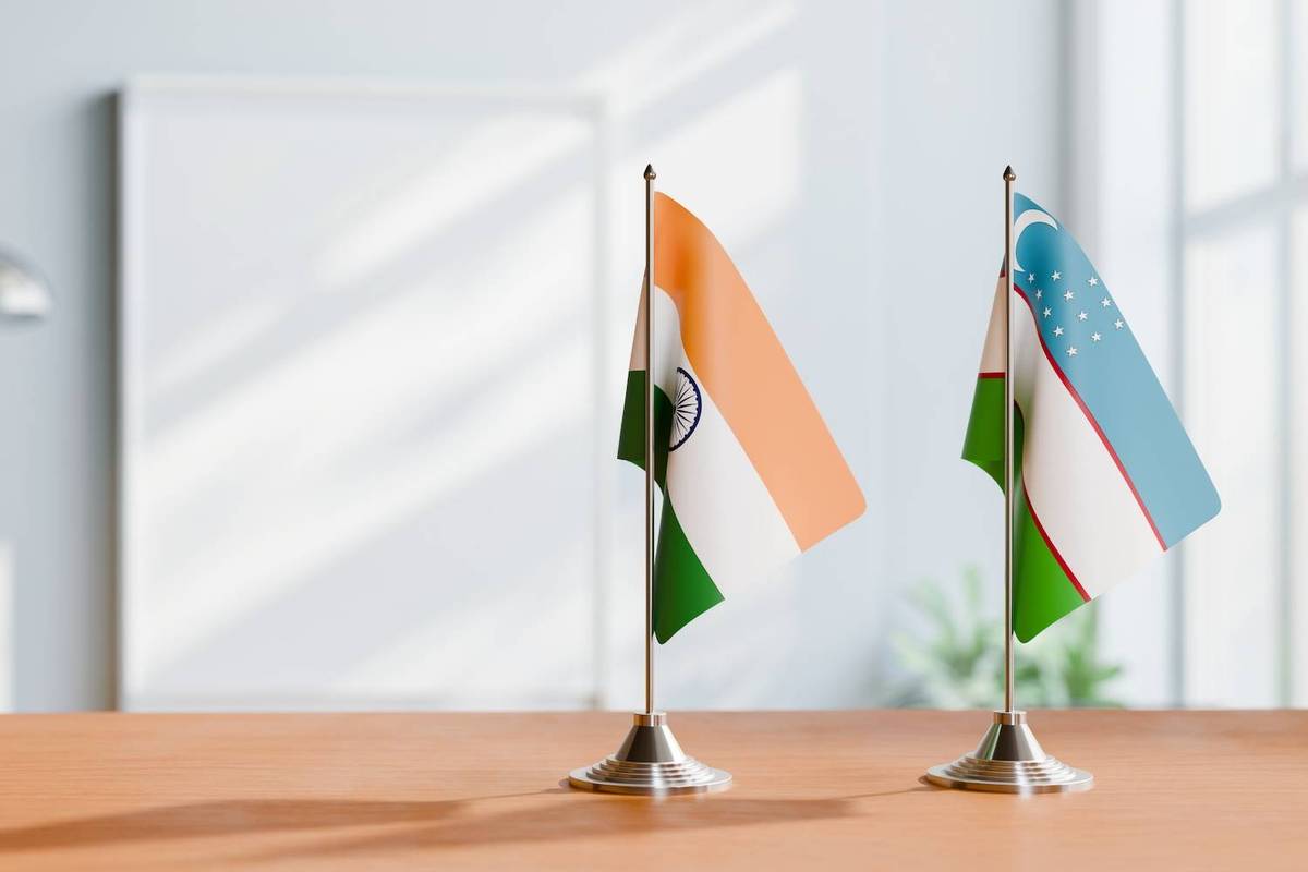 Two small tabletop flags, Indian and Uzbekistani, on a wooden surface with a blurred light background.