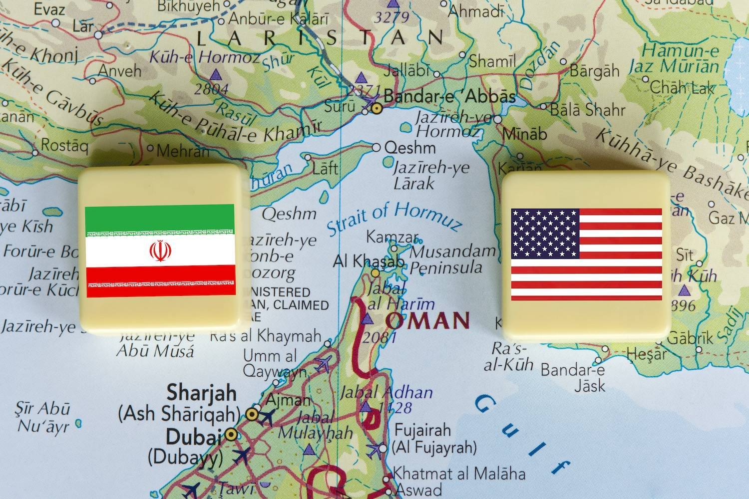 Two square blocks with Iranian and American flags placed on a map of the Strait of Hormuz.