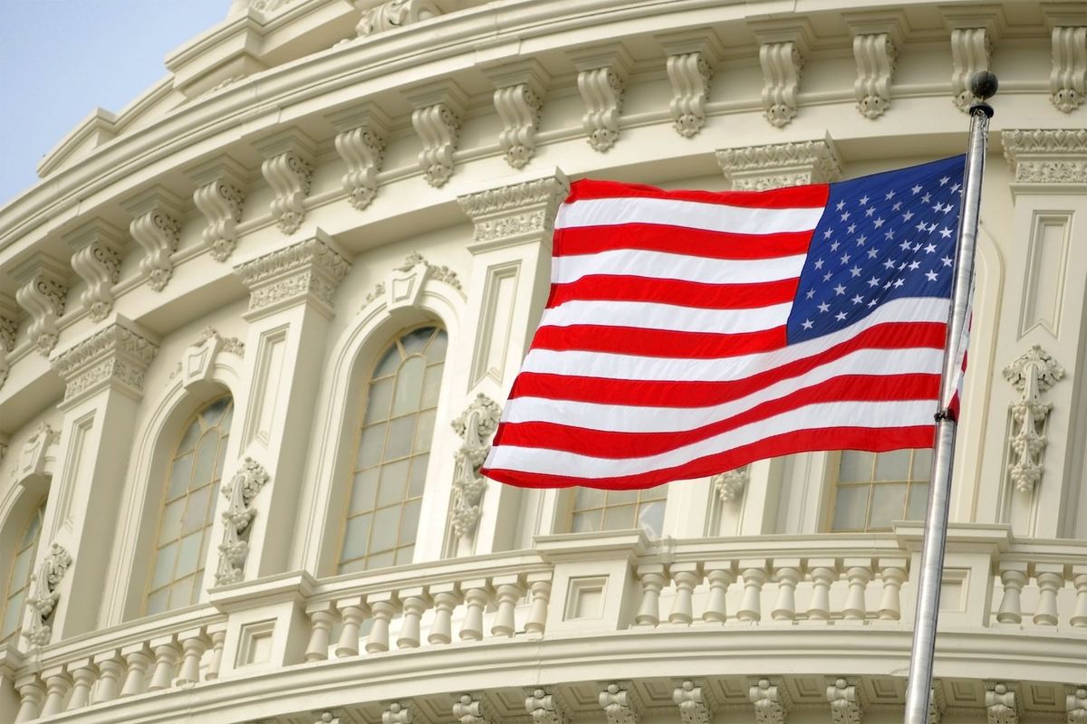 U.S. flag waving in front of a neoclassical building facade.