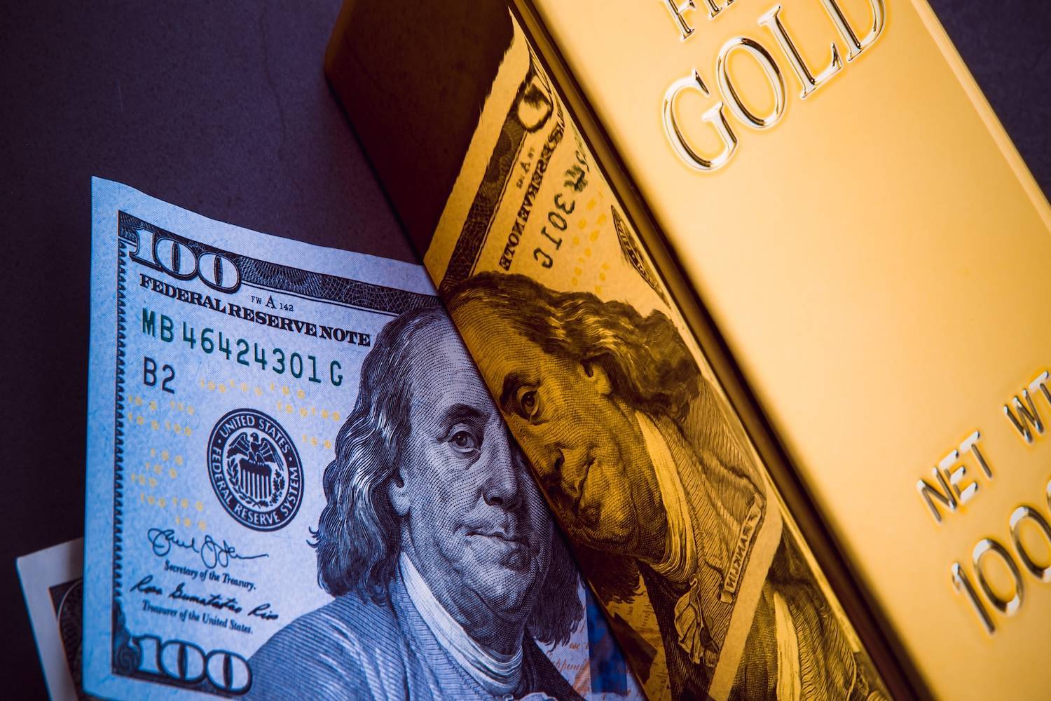 US$100 bill lies over a gold bar.