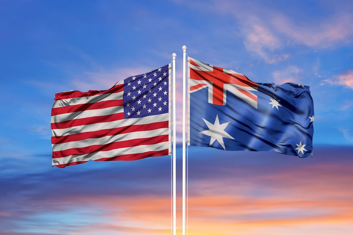 US and Australian flags waving against a colorful sunset sky.