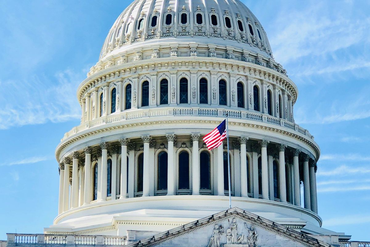 US Capitol dome with flag against a blue sky.