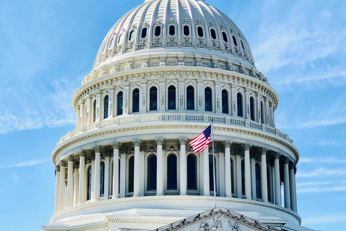 US Capitol dome with US flag against clear blue sky.