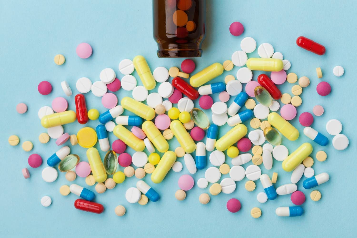 Various colorful pills and tablets scattered from a brown bottle on a blue background.