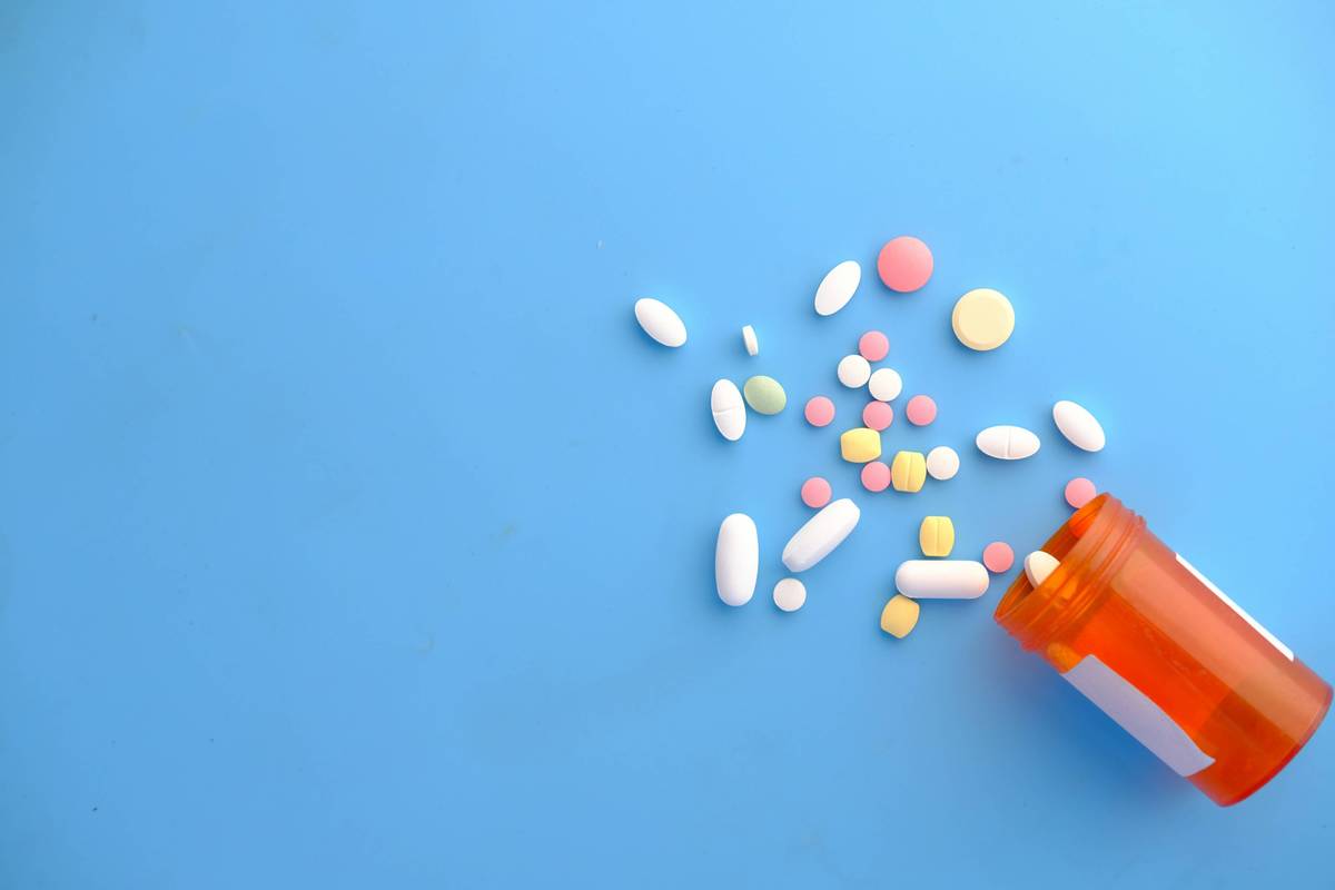 Various colorful pills and tablets spill from an orange prescription bottle onto a blue background.