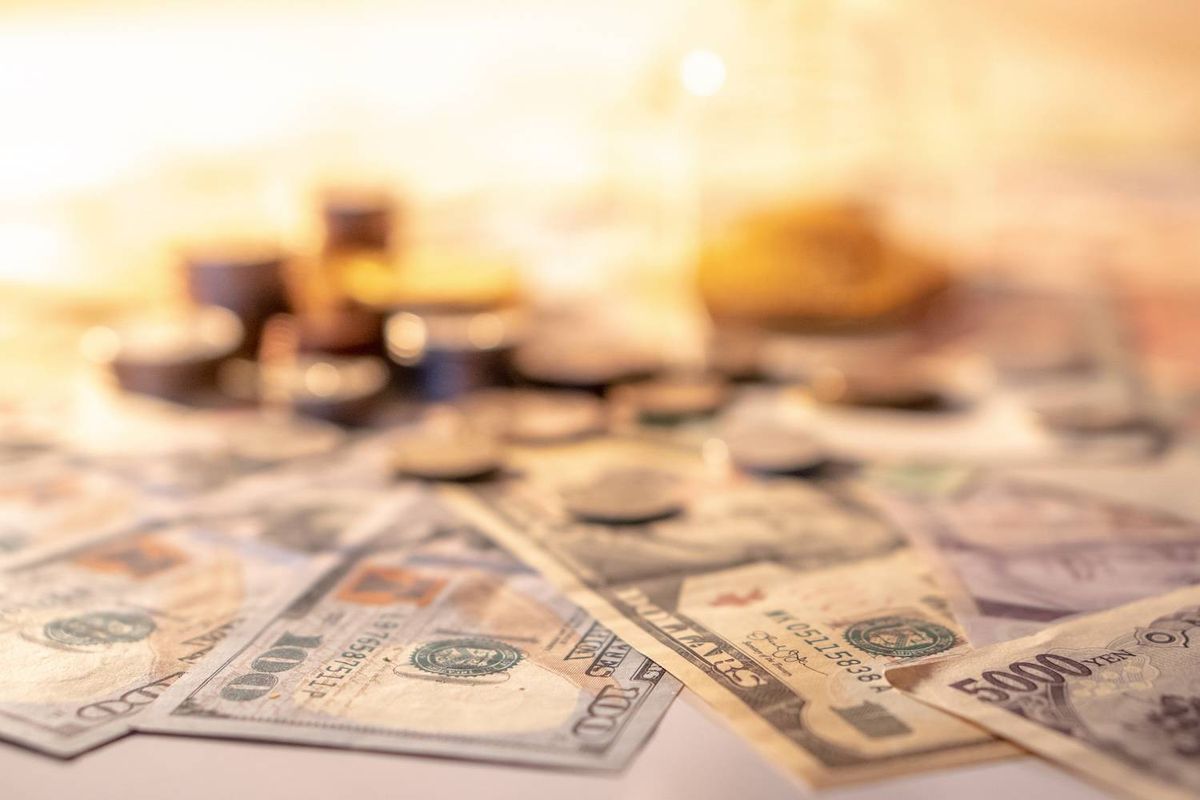 Various currency notes and coins scattered on a surface under warm lighting.