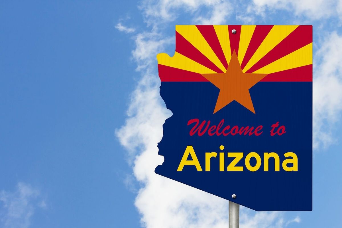 "Welcome to Arizona" sign with sunburst design against a blue sky background.