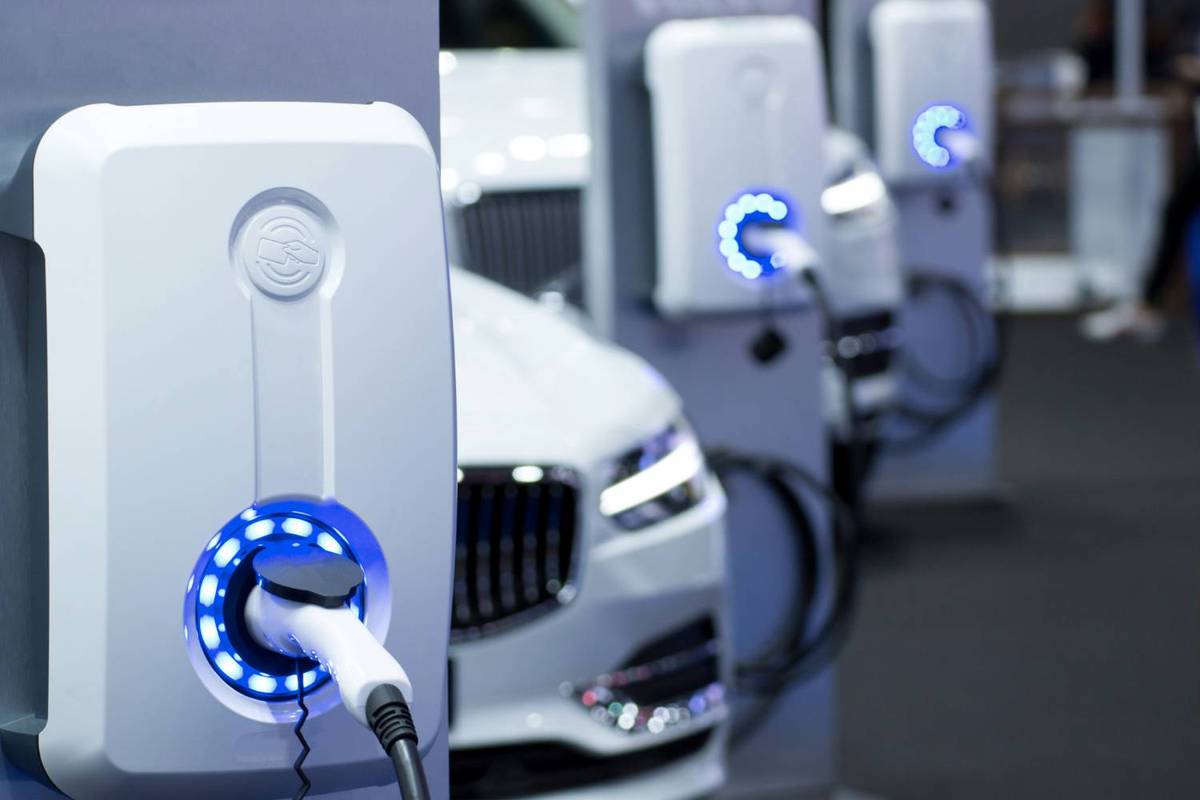 White electric cars plugged into charging stations with glowing blue rings over a dark showroom floor.