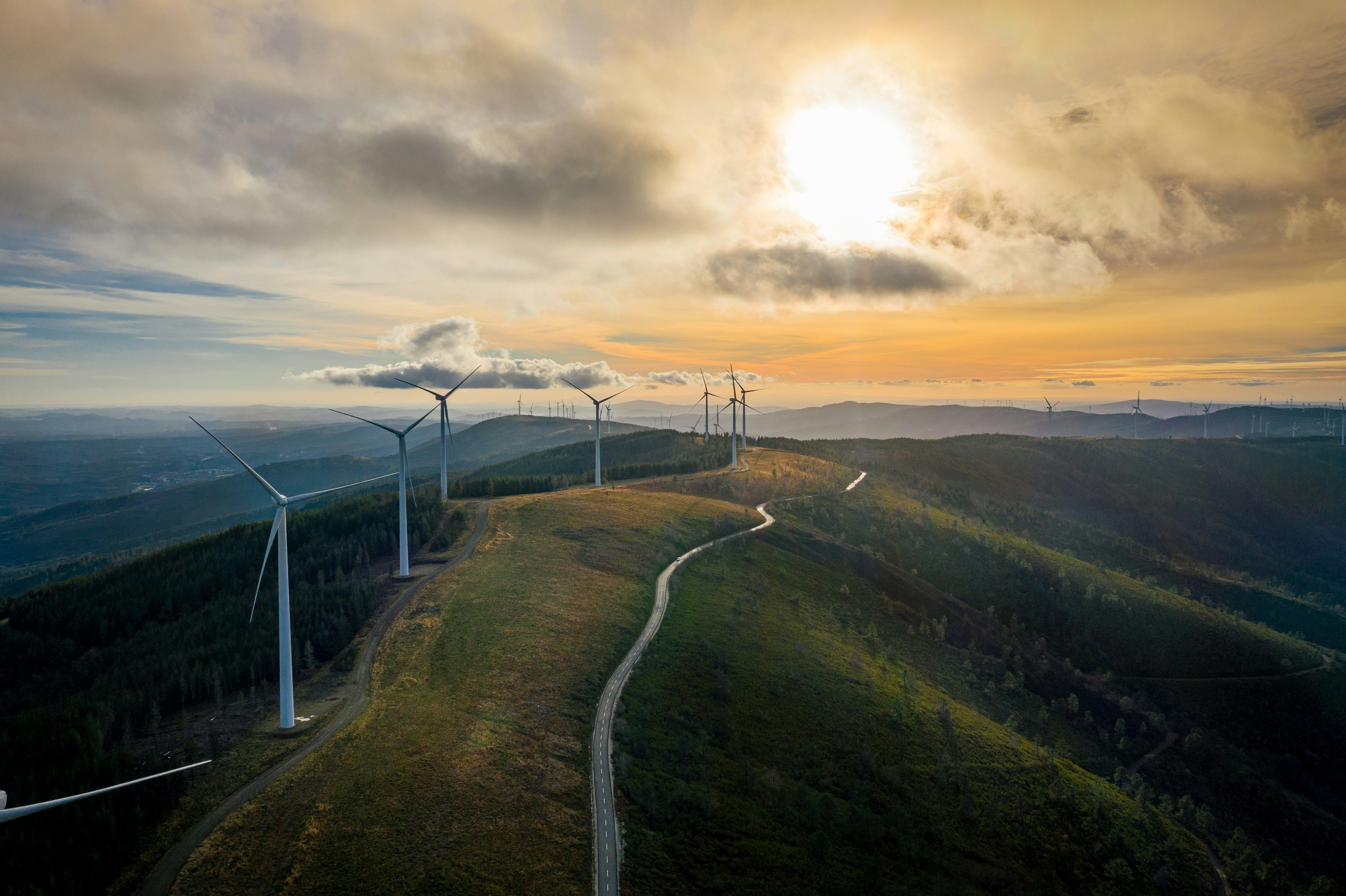 Wind turbines on a hill during sunset, with a winding path leading through the landscape.