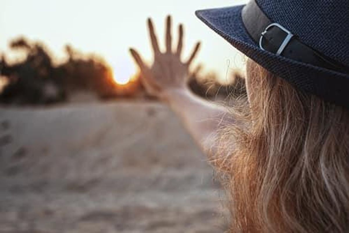 woman in a hat reaching hand to the sunrise on a beach