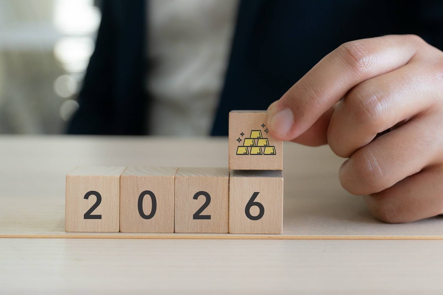 Wooden blocks showing a picture of gold bars and the year 2026.