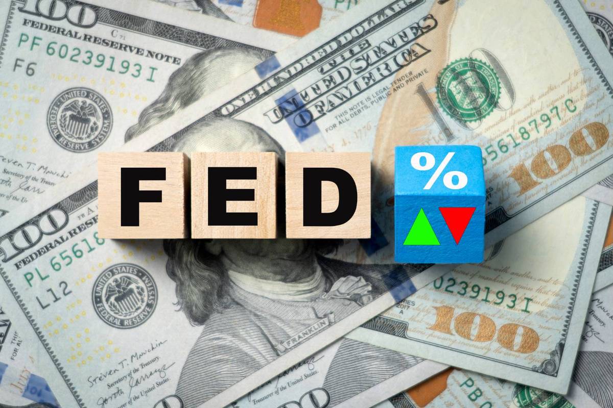 Wooden blocks spell "Fed" next to a blue block with symbols on scattered US$100 bills.