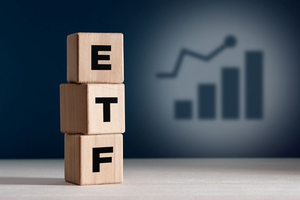 Wooden blocks spelling "ETF" with a graph shadow in the background.