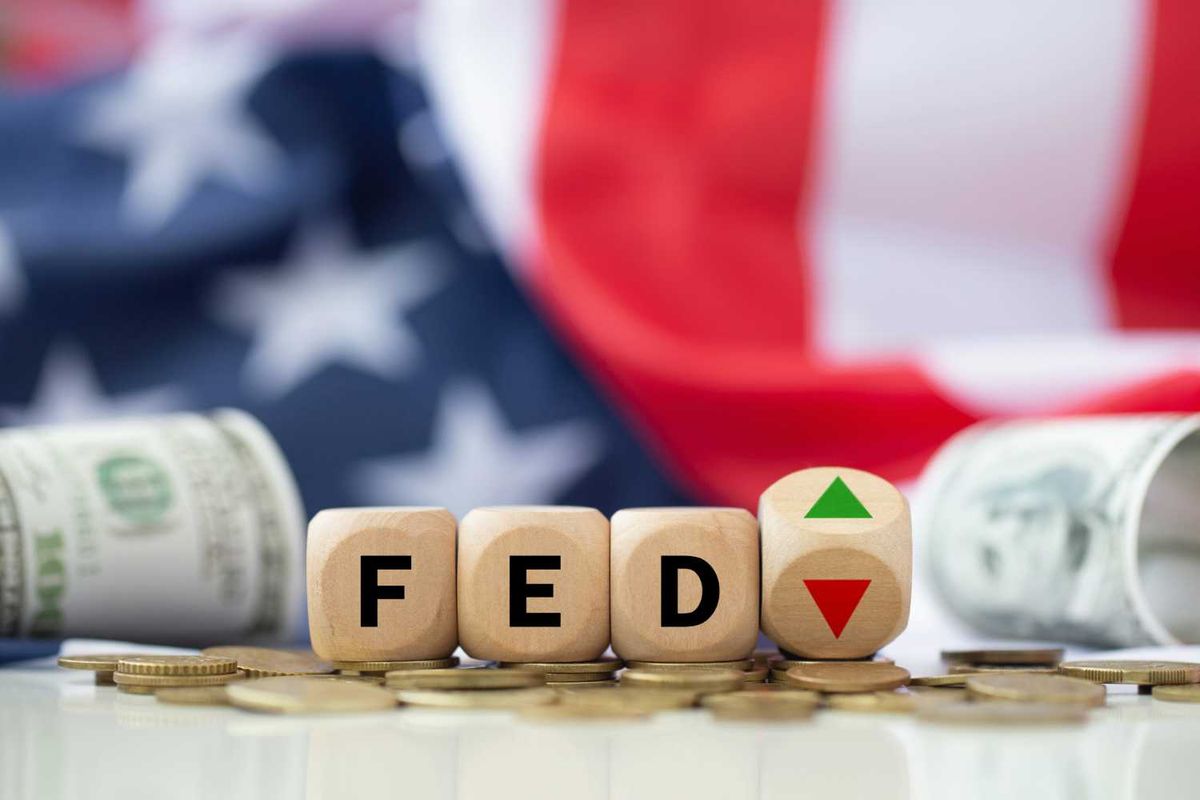 Wooden blocks spelling "Fed," arrows, coins and dollars on a US flag background.