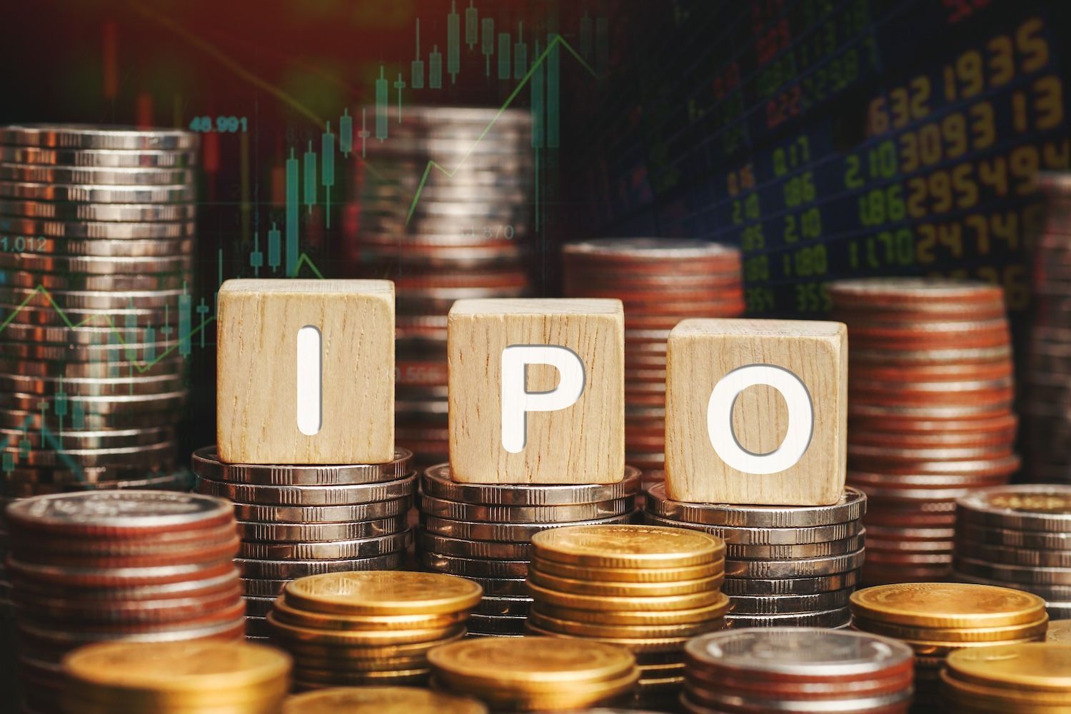 Wooden blocks spelling "IPO" on stacks of coins, with stock market data in background.