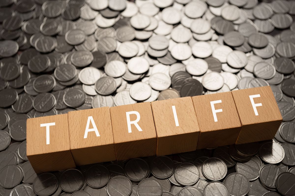 Wooden blocks spelling "tariff" on scattered coins background.