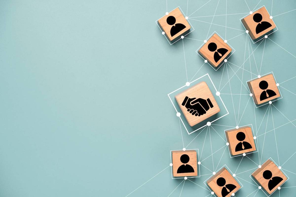 Wooden blocks with handshake and person icons connected with lines on a light teal background.