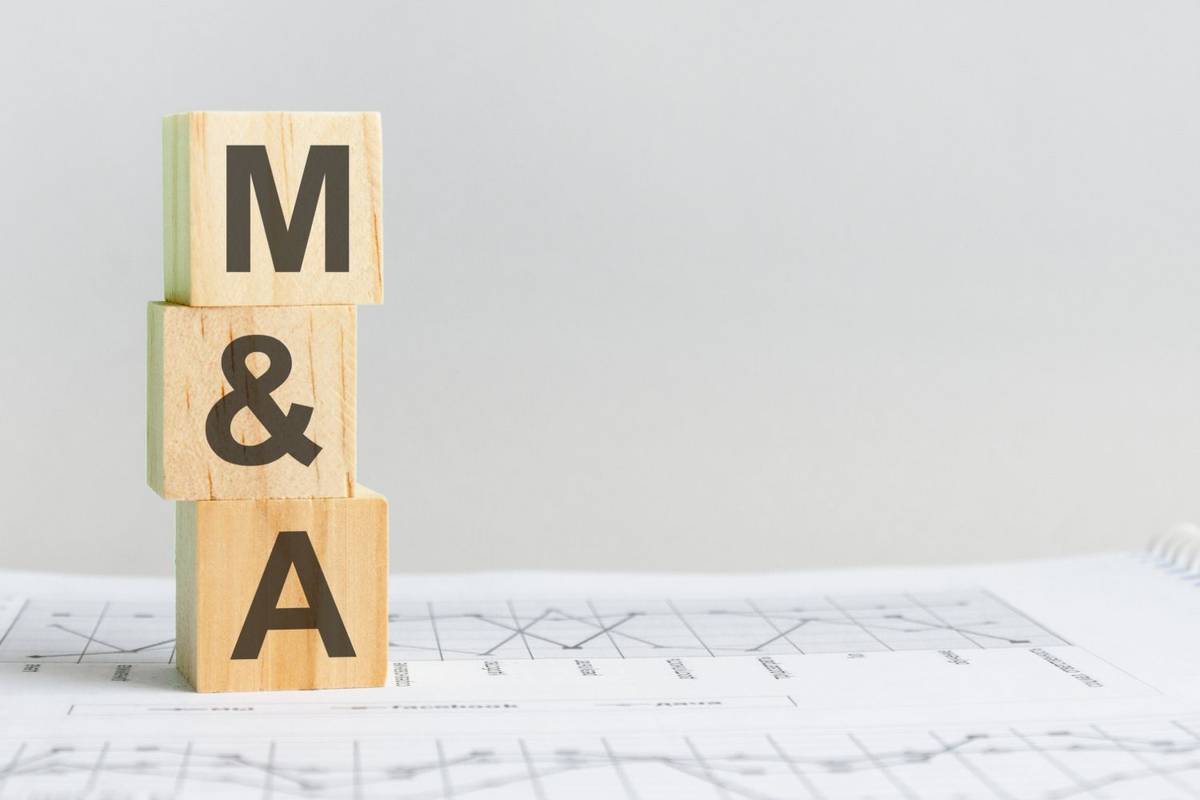 Wooden blocks with "M & A" stand vertically on white papers with charts, against a gray background.