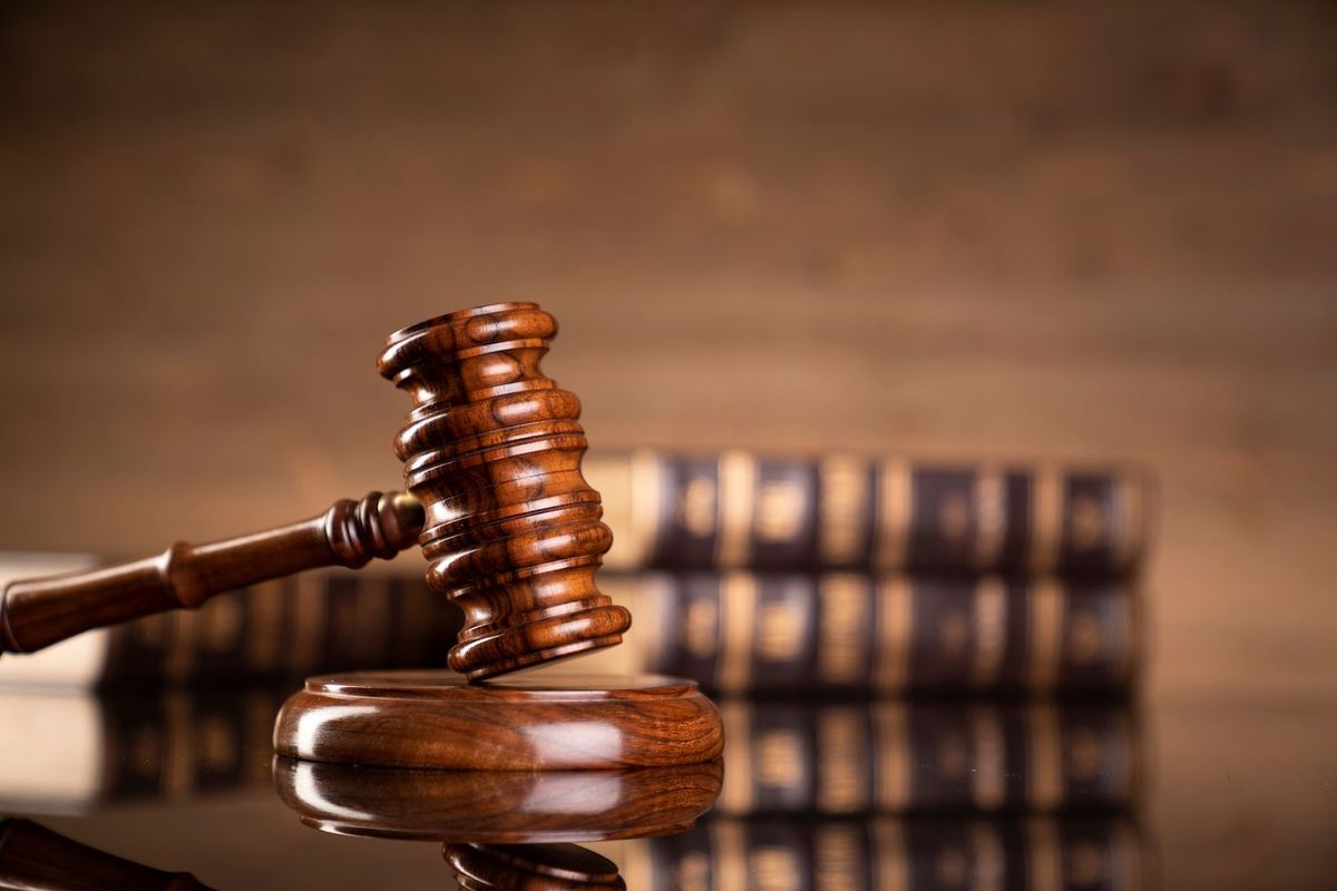 Wooden gavel and sound block with law books on reflective surface.
