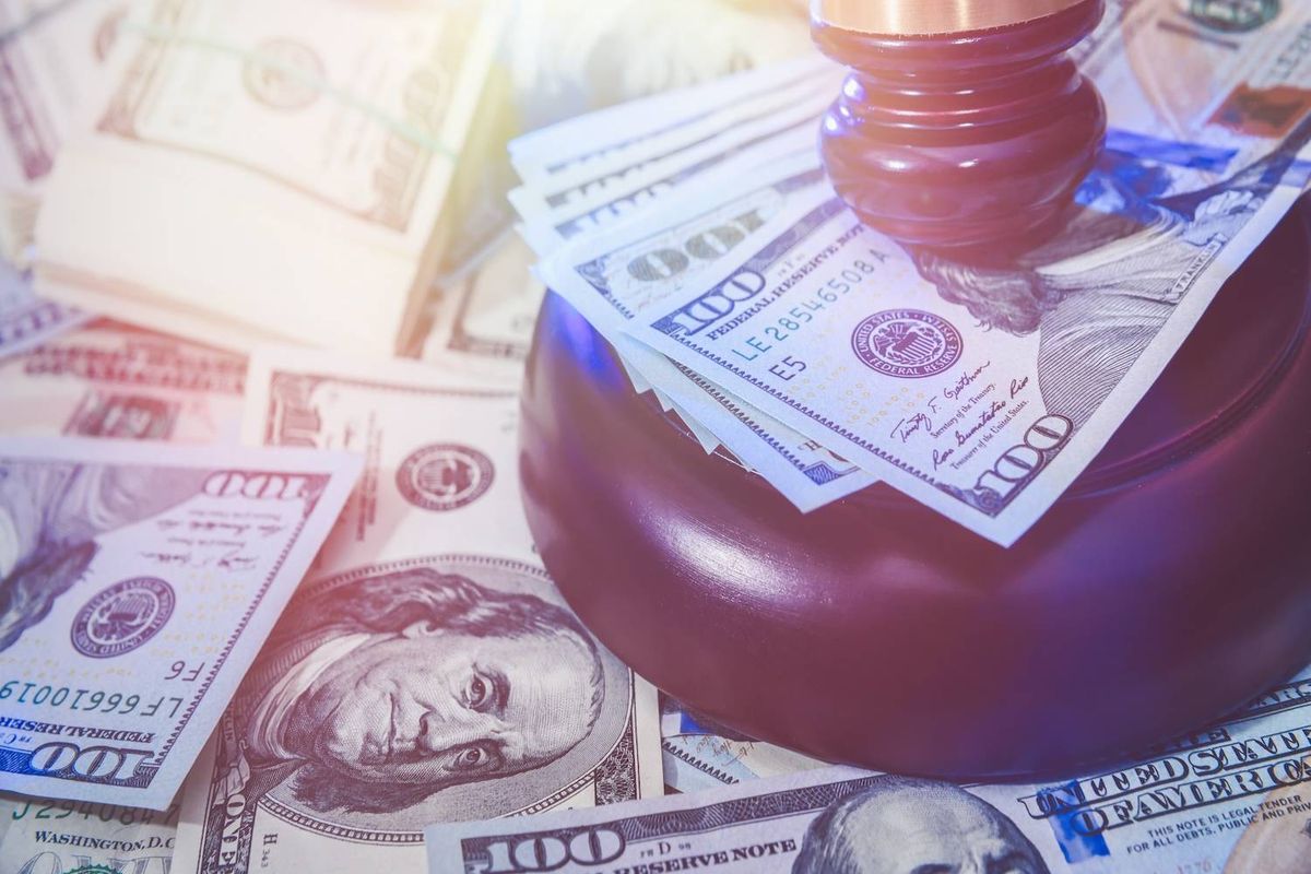 Wooden gavel rests on a pile of scattered and neatly stacked US$100 bills.