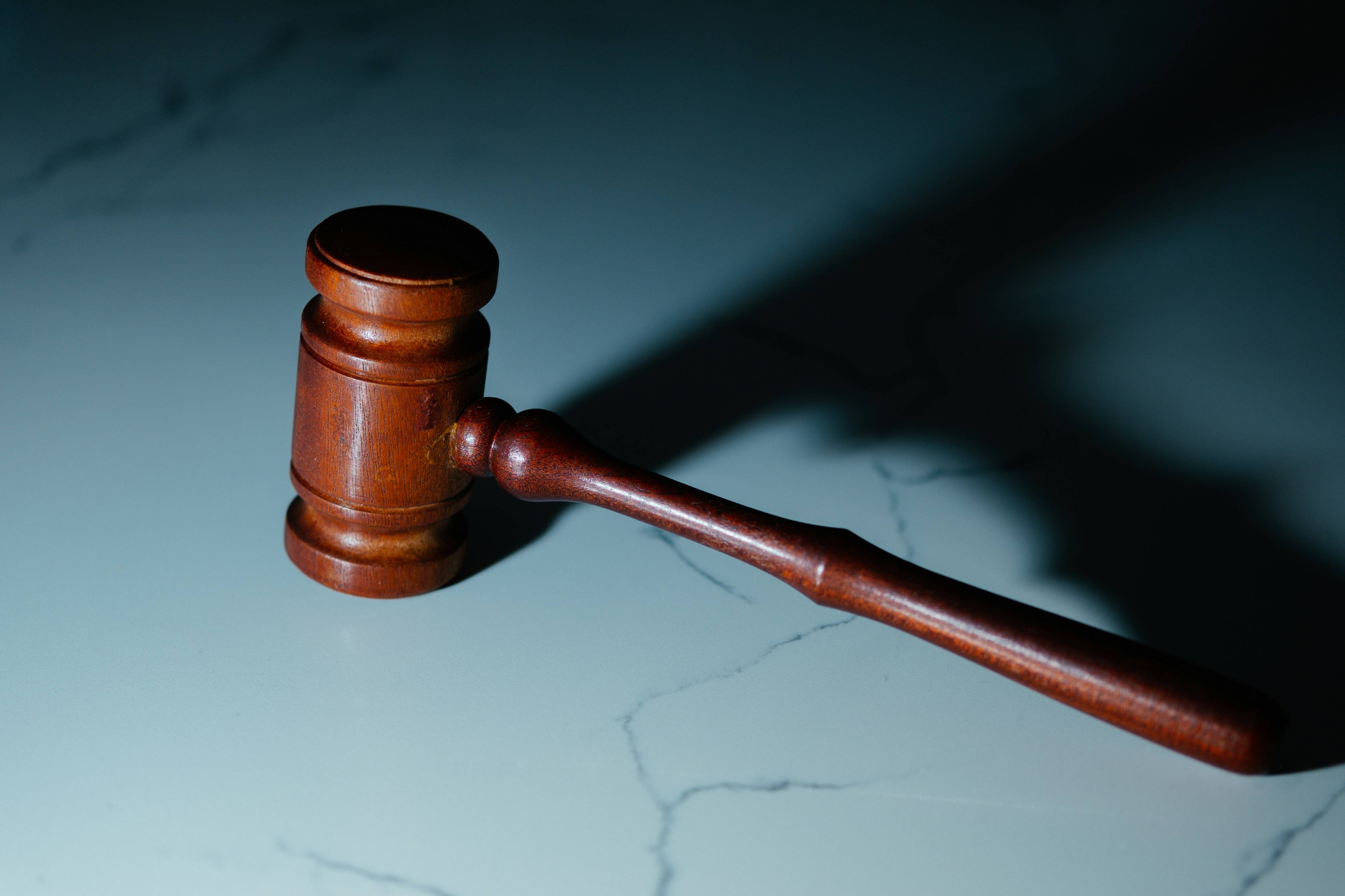 Wooden gavel with long handle rests on a gray marble surface, casting a shadow.