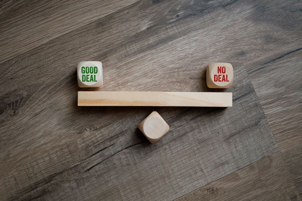 Wooden seesaw with "Good Deal" and "No Deal" blocks on each end.