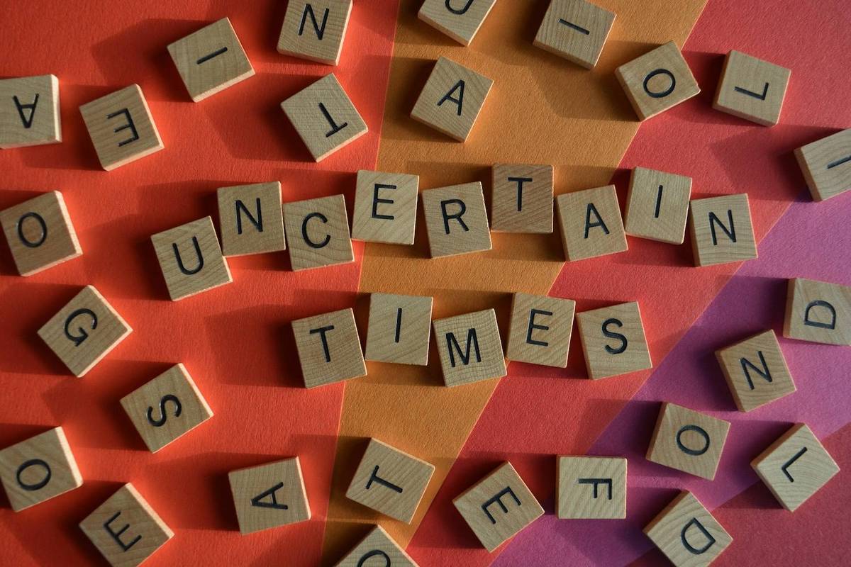 Wooden tiles spell "uncertain times" on colorful geometric background.