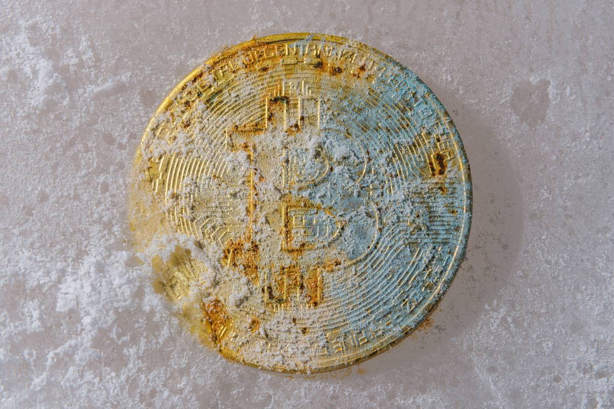 Worn Bitcoin partially covered in white dust on a light surface.