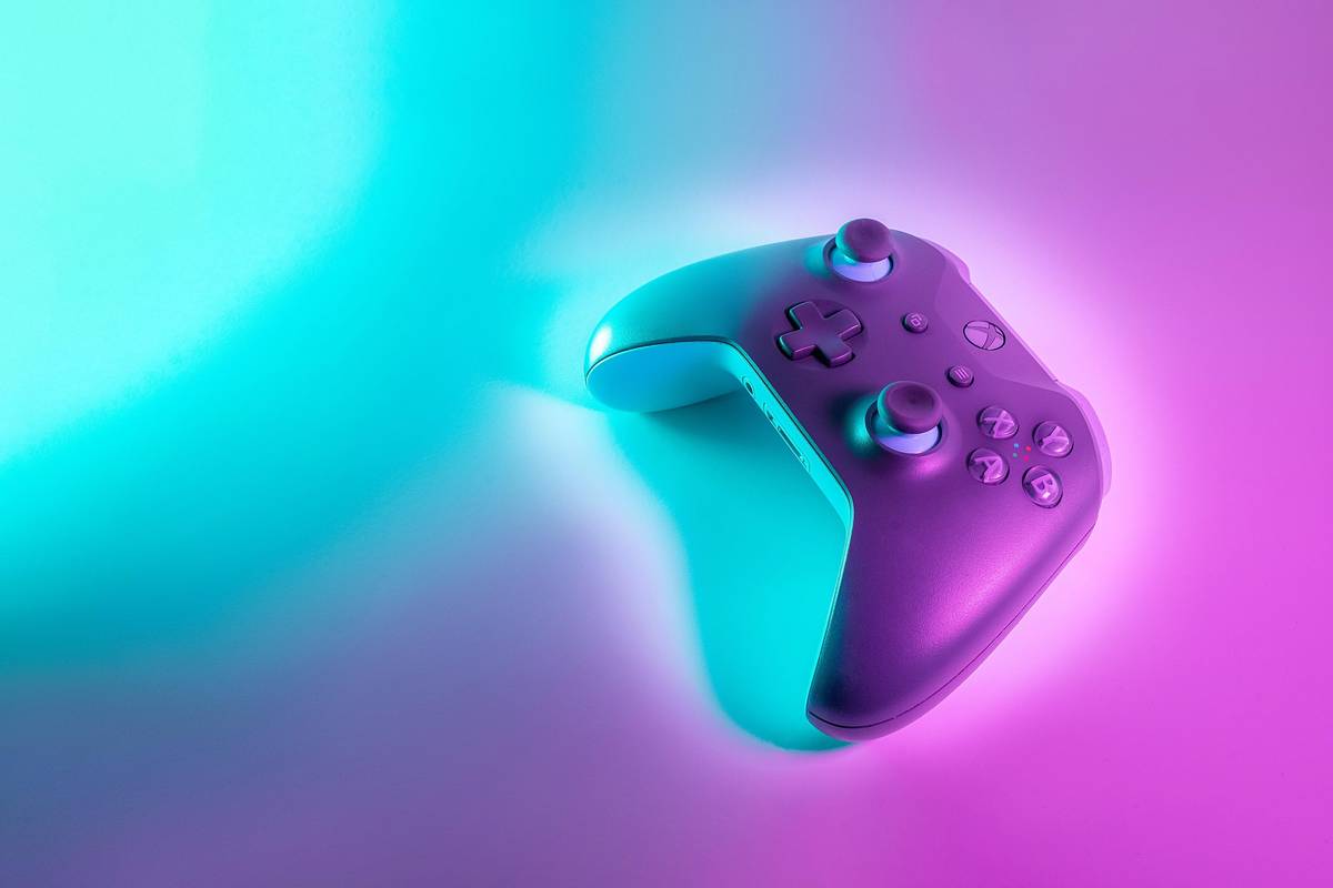 Xbox brand game controller illuminated by pink and turquoise lighting.