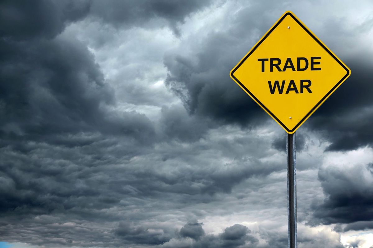 Yellow sign saying "trade war" against cloudy sky.