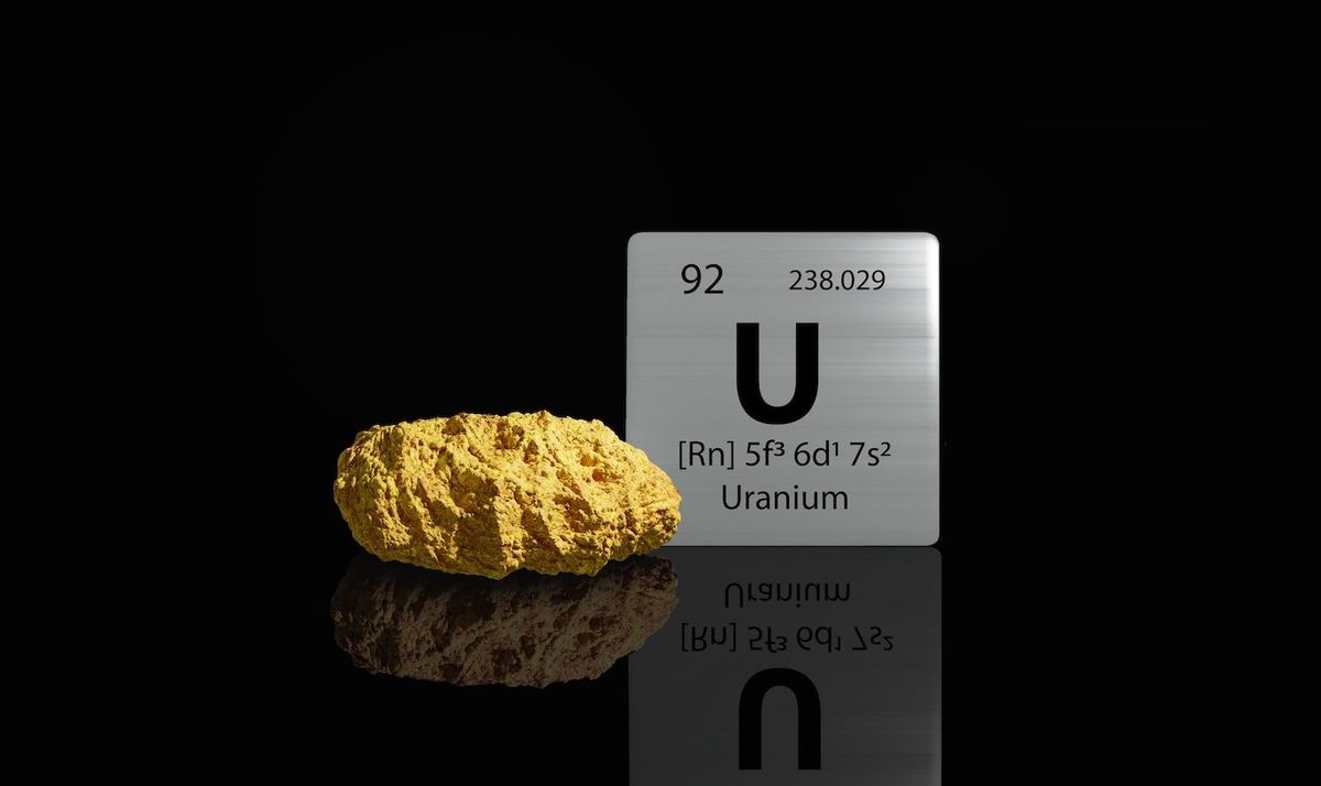 Yellow uranium ore with periodic table symbol on black reflective surface.